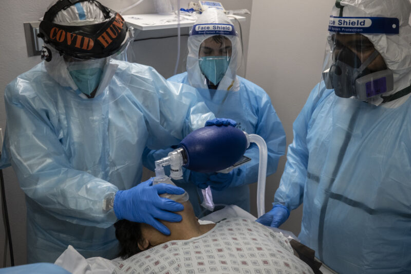 Medical workers in protective gear apply a breathing apparatus to a recline patient.