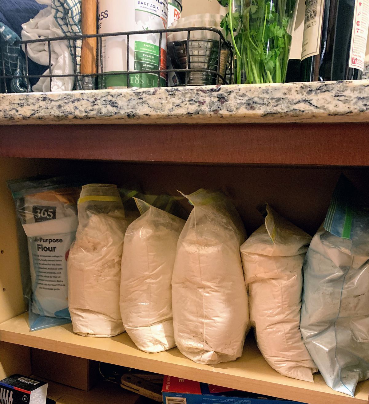 Ziplocked bags of flour lined up in a kitchen cupboard.