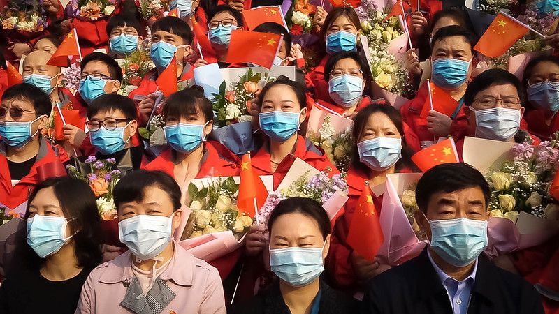 A crowd of Chinese people wearing masks and holding the Chinese flag.