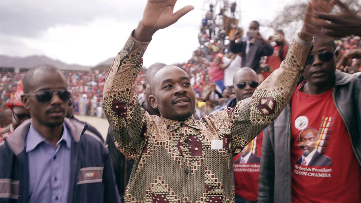 Zimbabwean presidential candidate Nelson Chamisa stands in the midst of a crowd, hands upraised to greet the people, flanked by bodyguards.