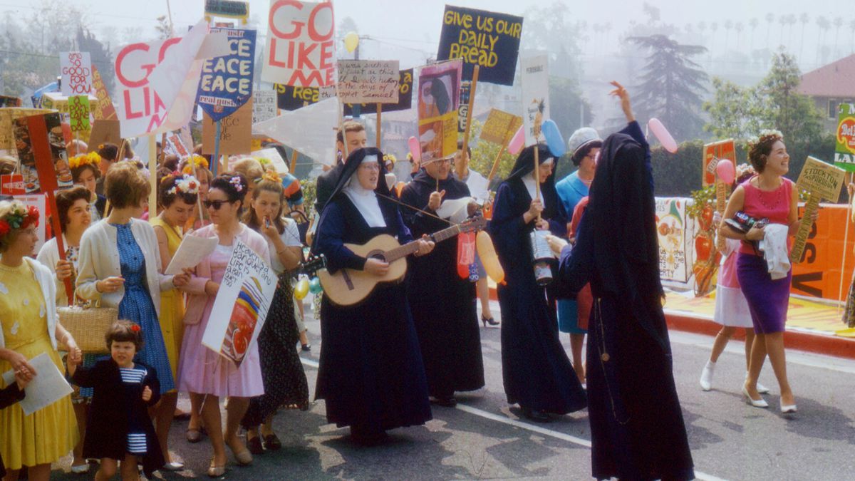 A group of nuns holding protest signs and guitars lead a protest.