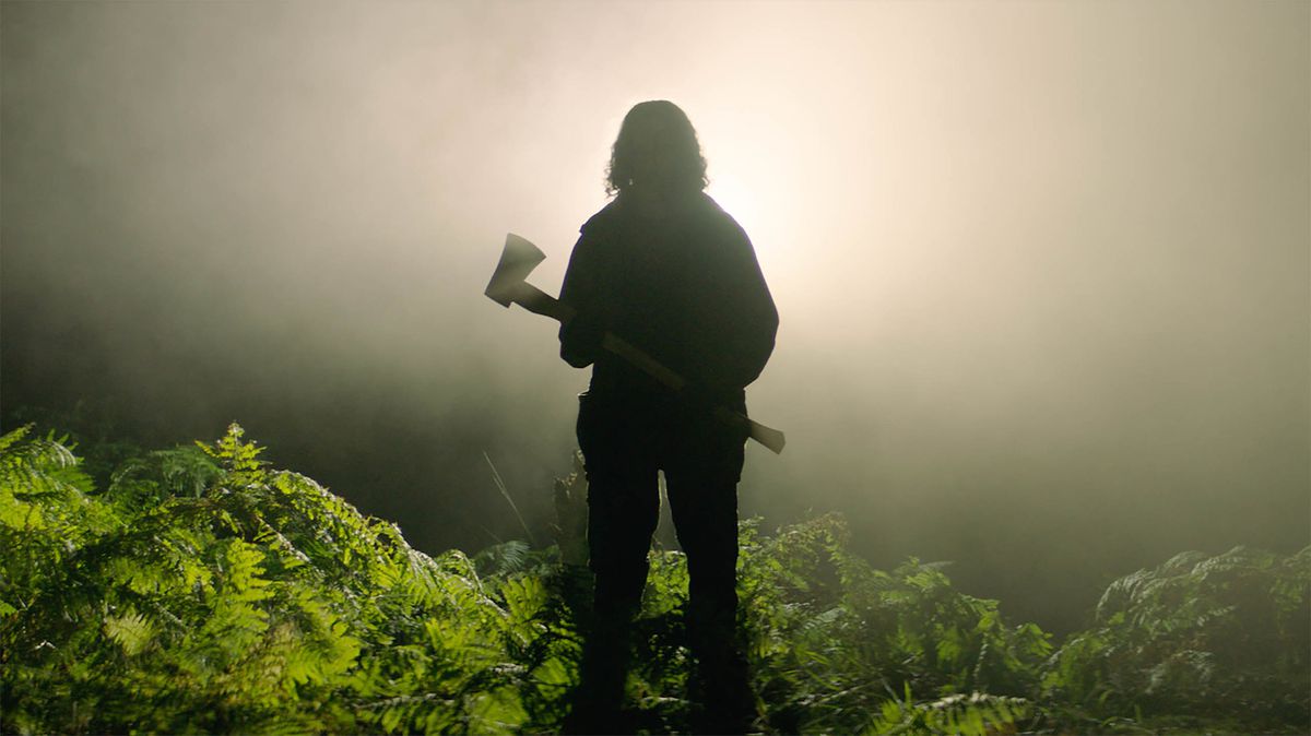 A man silhouetted against a bright, foggy light, holding an axe.